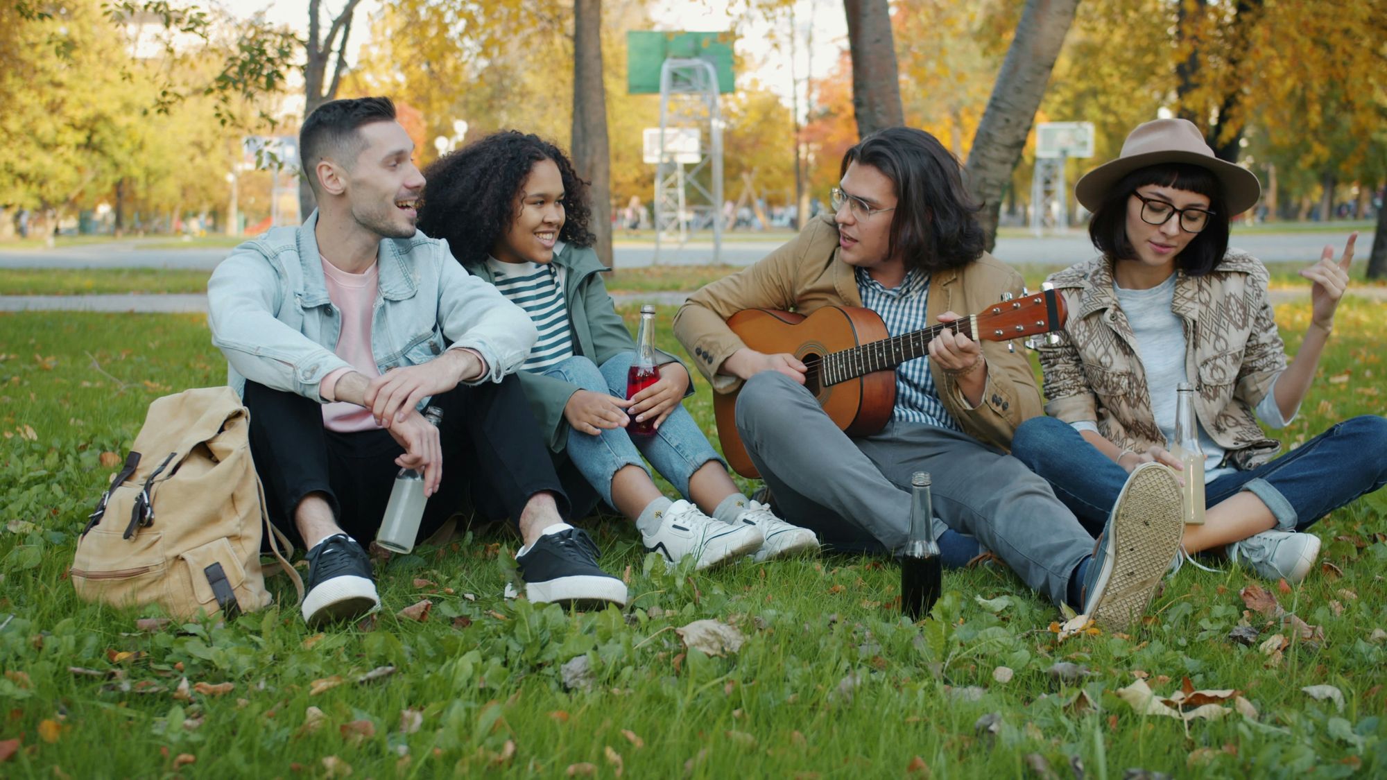Youth sitting together outdoors, one playing guitar, laughing